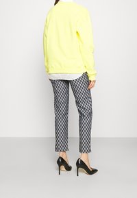 Suéter amarillo, pantalones de cuadros grises, tacones altos negros. Corte relajado, puños acanalados, tela estampada, forma entallada.