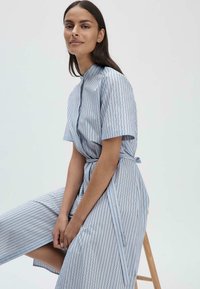 Abito azzurro chiaro con strisce verticali di blu scuro e oro. Maniche corte, colletto alto e una cintura da annodare in vita.
