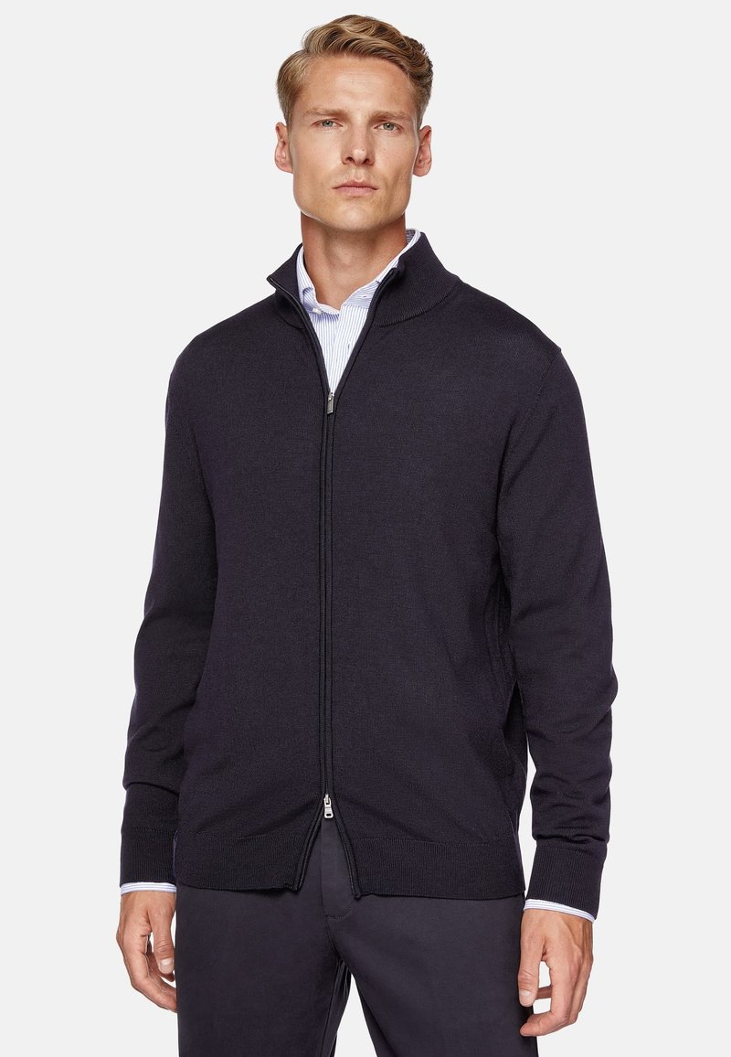 Navy zip-up sweater with a textured knit, ribbed cuffs, and collar. Features a slim fit and is paired with a light striped shirt underneath.