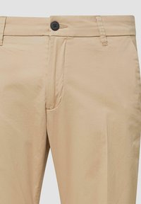 Beige Herrenhose mit Knopfverschluss an der Front, Gürtelschlaufen und Seitentaschen, aus glattem Stoff gefertigt.