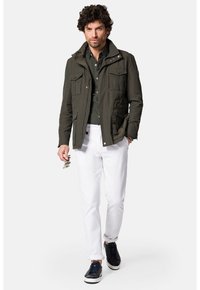 Jasnozielona, lekkie kurtka z wieloma przednimi kieszeniami, zestawiona z ciemną koszulą i białymi spodniami, uzupełniona granatowymi sneakersami.