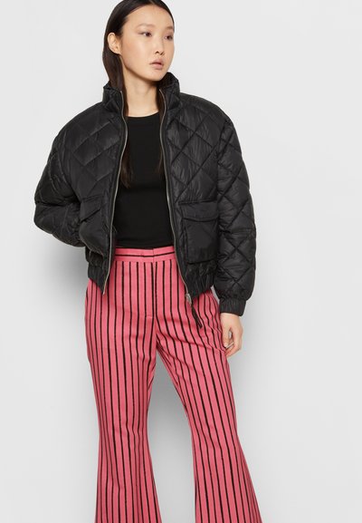 Casaco bomber preto acolchoado com gola alta, fecho de zíper e dois bolsos frontais, combinado com calças largas listradas em rosa.