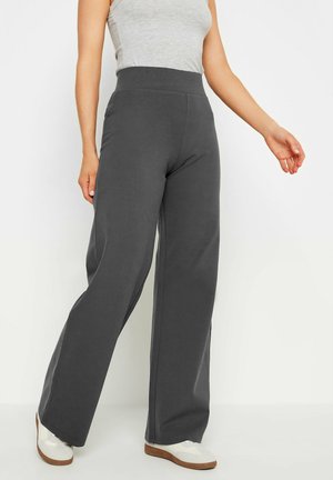 Woman wearing high-waisted dark gray wide-leg pants, gray sleeveless top, and white sneakers standing against a white background.