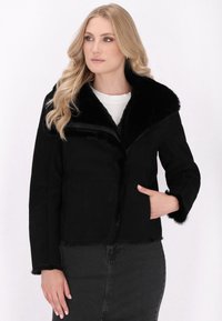 Veste en fausse fourrure noire avec un large col, des poches latérales et une texture douce. Les manches et l'ourlet ont des accents en fourrure.