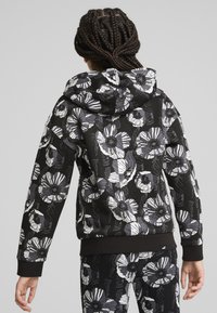 Huooded sweatshirt med svart bakgrund som har stora vita och grå blommönster. Ribbad ärmar och fåll, mjuk tygstruktur.