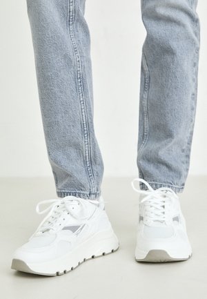 Baskets blanches avec des accents gris, dotées d'une tige en mesh, d'un bout rond et d'une semelle épaisse en caoutchouc. Portées avec un jean slim bleu clair.