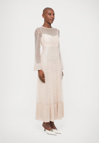 Duga, prozirna haljina svijetlosmeđe boje s ukrasima od perlica, prilagođenim gornjim dijelom, lepršavim rukavima i plisiranom suknjom. Bijele cipele na visoku petu.