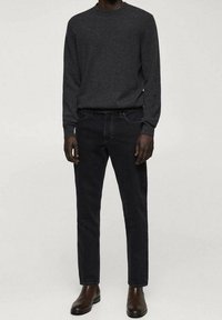 Suéter gris oscuro con cuello redondo, combinado con jeans de mezclilla negros. El modelo lleva botas de cuero marrón hasta el tobillo. Tejido texturizado, diseño ajustado.