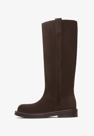 Braune kniehohe Stiefel aus einem glatten, samtartigen Material mit flacher Sohle, die ein nahtloses Design und eine einfache Seitenpartie aufweisen.