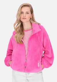 Leuchtend pinke Fleecejacke mit Reißverschluss, hohem Kragen und gerippten Bündchen, getragen über einem rosa-weiß gestreiften Hemd. Weiche Textur, oversized Passform.