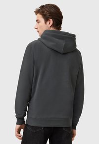 Dunkelgrauer Hoodie mit weicher Textur, im Pullover-Design, großer Kapuze und gerippten Bündchen und Saum. Getragen mit dunklen Jeans.