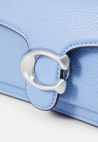 Gros plan d’un sac en cuir bleu clair texturé avec une fermeture en métal argenté en forme de C et des bords cousus assortis.