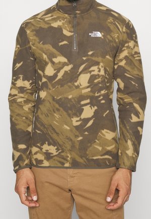 Mens camo-patterned pullover fleece with a quarter zip and The North Face logo on chest, paired with light brown pants.