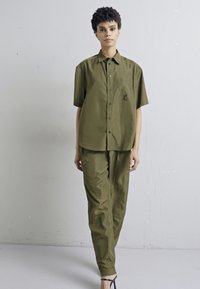 Olijfgroen, kortomhuls shirt en bijpassende broek, gemaakt van soepel, lichtgewicht materiaal; heeft knopen en een borstzak.
