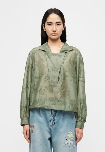 Πράσινο διάφανο πουκάμισο με κεντήματα λουλουδιών και σχεδιασμό V-λαιμόκοψη. Μακριά μανίκια με ελαστικά τελειώματα. Συνδυασμένο με ανοιχτό μπλε τζιν παντελόνι με μπαλώματα.