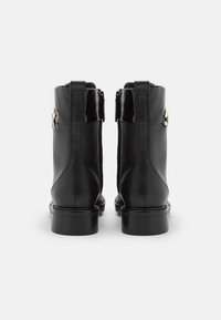 Stivaletti alla caviglia in pelle nera con un dettaglio lucido in vernice sulla parte superiore, dotati di cerniera laterale e particolare in metallo color oro.