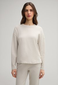 Light gray long-sleeve cotton top with a round neck, dropped shoulders, and side buttons. The fabric has a smooth, soft texture.