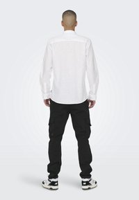 Camisa blanca de manga larga con dobladillo redondeado y detalles de botones, combinada con pantalones cargo negros que cuentan con bolsillos laterales y un ajuste holgado.