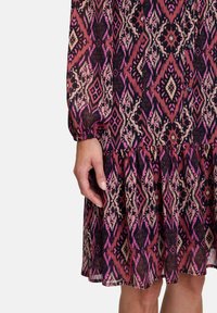 Colorful printed dress featuring a geometric pattern in shades of pink, purple, and cream, with a flowing tiered skirt and loose sleeves.