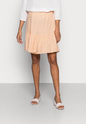 Jupe florale orange clair avec un ourlet volanté, en tissu léger et avec un motif subtil ; associée à des sandales à talons blocs rose clair.