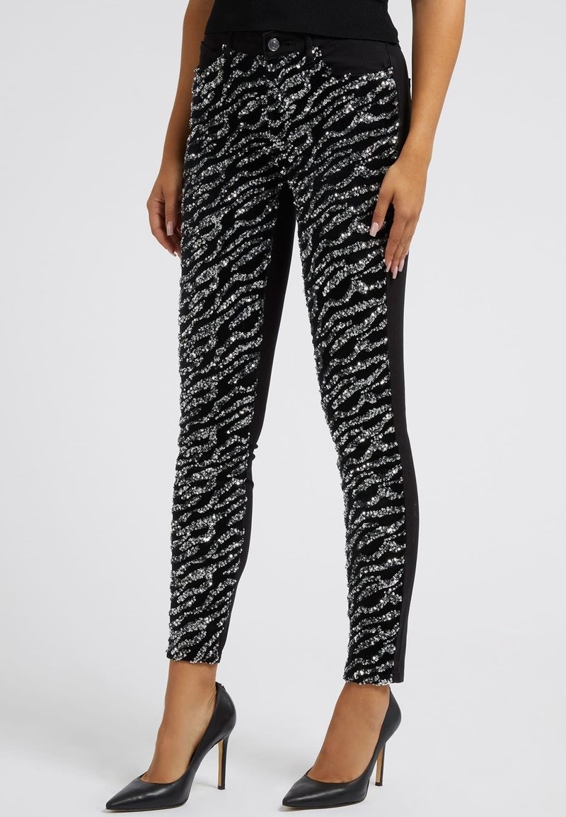 Pantalones negros con un patrón de rayas de cebra texturizadas y detalles en plateado. El diseño ajustado incluye un cierre frontal con botón y bolsillos.