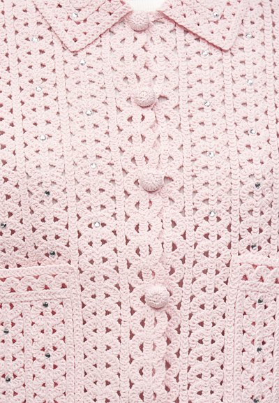 Απαλό ροζ πλεκτό ζακέτα με στρογγυλά κουμπιά και μικρές διαφανείς στρας που διακοσμούν το σχέδιο και δύο μπροστινές τσέπες.
