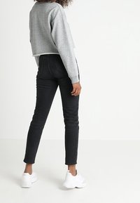 Felpa grigia corta, jeans neri slim-fit e sneaker bianche. Le caratteristiche includono polsini a costine e un design semplice. Il tessuto appare morbido.