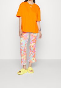 Oranžové bavlněné tričko, vícbarevné kalhoty s květinovým vzorem a žebrovanou texturou a žluté nazouvací boty s větracími otvory.