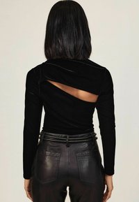 Czarny zwiewny top z długim rękawem i drapowaną tylną częścią, z otwartą sekcją. W połączeniu z czarnymi skórzanymi spodniami o wysokim stanie z kieszeniami.