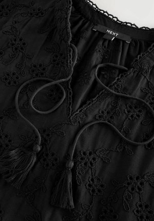 Black embroidered blouse with floral patterns, featuring a V-neckline, adjustable ties, and tassel accents. Soft fabric with textured details.