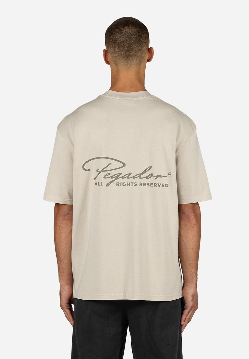 Vaaleanbeige puuvillainen t-paita lyhyillä hihoilla, selässä tummanharmaa logo. Rentojat sekä yksinkertainen muotoilu, ilman kuvioita.