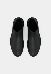 Une paire de chaussures en cuir noir à enfiler avec des orteils ronds et des languettes à l'arrière, vue de dessus sur un fond blanc.