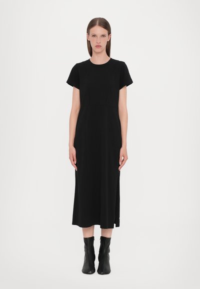 Robe noire à mi-mollet avec manches courtes et encolure ronde. Fabriquée dans un tissu texturé avec des détails de couture verticaux et des fentes sur les côtés.