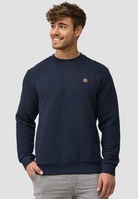 Marineblauwe sweatshirts met textuur, ronde hals, ribgebreide manchetten en een klein bruin logo-accent op de borst. Slank ontwerp met een zachte afwerking.