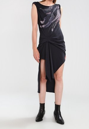 Vestido negro con detalle anudado en la cintura, dobladillo asimétrico y estampado floral abstracto en el frente. Combinado con botines negros.