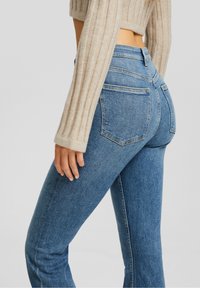 Fitted blue denim jeans with a smooth texture, a mid-rise waist, and classic back pockets. The garment features a slight stretch for comfort.
