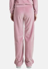 Rosa Samt-Loungehosen mit lockerem Schnitt. Weicher Stoff, elastischer Bund und leicht ausgestellte Beine, die sich an den Knöcheln verjüngen.
