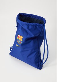 Sac à dos bleu avec un tissu doux, orné du blason du FC Barcelone et du logo Nike en jaune. Ouverture supérieure avec cordon et resserrement.