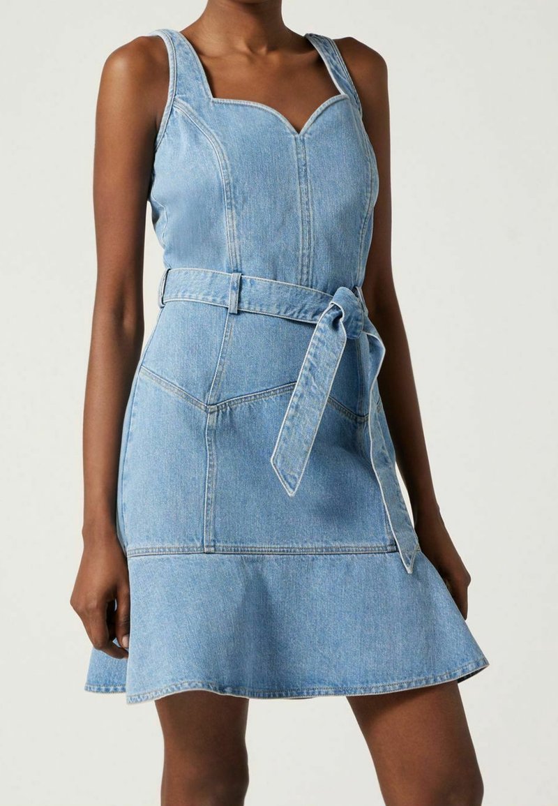 Vaaleansininen farkkumekko, jossa istuva yläosa, leveät olkaimet ja liehuva hame. Mekossa on vyötäröllä vyö ja kontrastipistot yksityiskohtina.