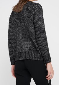 Svart och vit stickad tröja med lös passform, ribbad nederkant och långa ärmar. Texturerat mönster ger visuell variation.