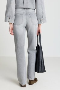 Graue, hoch taillierte Schlaghosen aus Denim mit ausgewaschener Textur, ausgestattet mit zwei Gesäßtaschen; kombiniert mit einer schwarzen Tragetasche und braunen Schuhen.