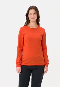 Langärmliges orangefarbenes T-Shirt aus glattem Material, mit Rundhalsausschnitt und dezentem aufgedrucktem Logo auf der Vorderseite. Kombiniert mit dunklen Hosen.