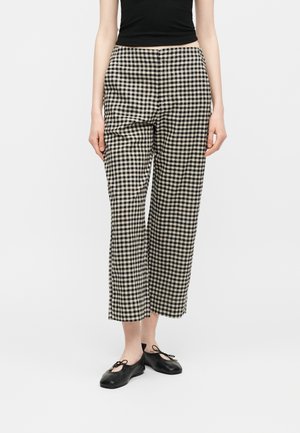 Άτομο που φοράει ασπρόμαυρο καρό παντελόνι φαρδύ, μαύρη αμάνικη μπλούζα και μαύρα μπαλαρίνια με κορδόνια.