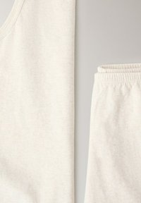 Gros plan sur un débardeur en tissu blanc doux et un short à taille élastique sur un fond neutre, mettant en valeur la texture et les coutures.