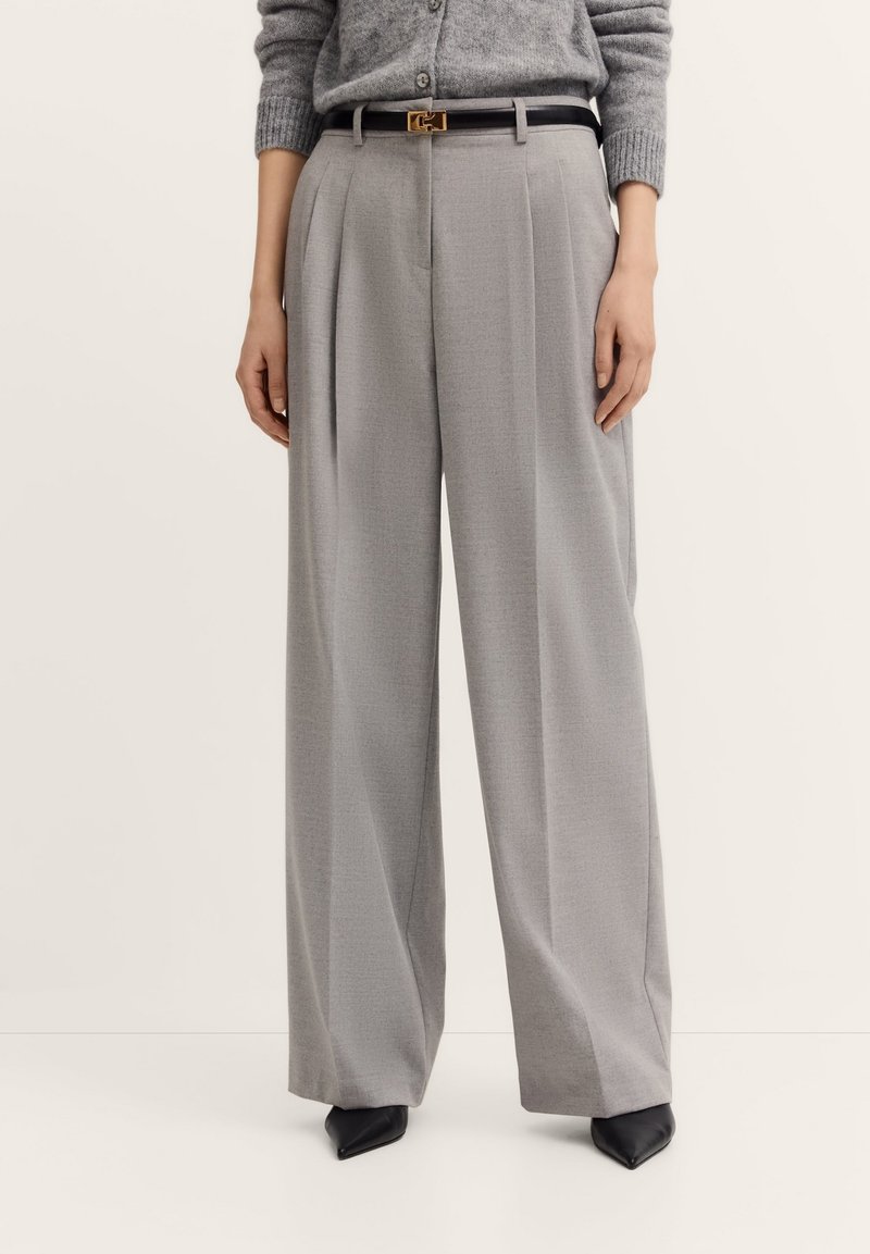 Hellegraue, weite Hose aus strukturiertem Stoff, mit vorderen Falten, einem schwarzen Gürtel mit einer Schnalle aus goldfarbenem Metall und spitzen schwarzen High Heels.