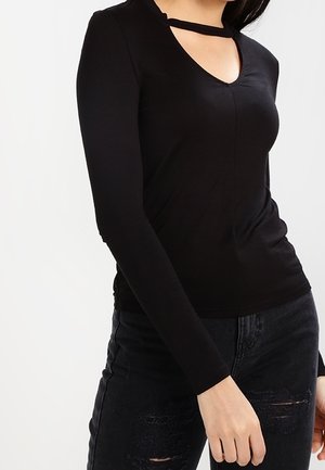 Top nero a maniche lunghe con scollo a V e dettaglio tagliato nella parte anteriore. Realizzato in tessuto morbido, ha una forma aderente e si abbina a jeans neri strappati.