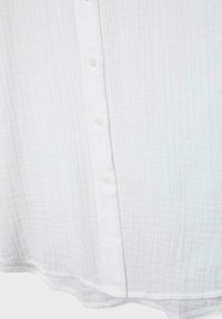 Davanti di una camicia in tessuto bianco stropicciato con una fila verticale di tre piccoli bottoni bianchi e un orlo leggermente curvo.