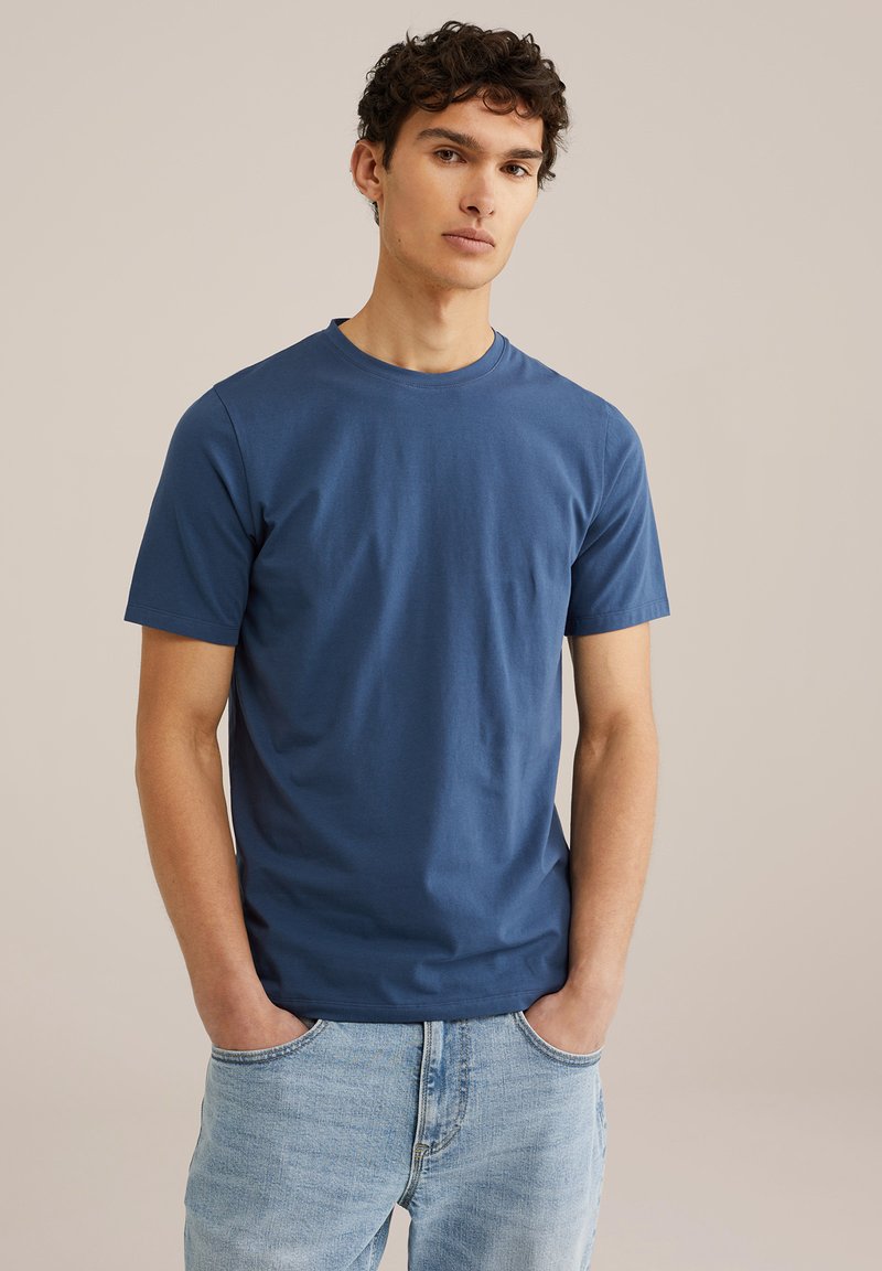 Modra kratka majica s kratkimi rokavi iz bombaža, z okroglim izrezom in gladko teksturo, v kombinaciji s svetlimi denim hlačami.