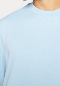 Sudadera azul claro con cuello redondo, hecha de tela de algodón suave. La textura es lisa con un sutil patrón acanalado en el escote.