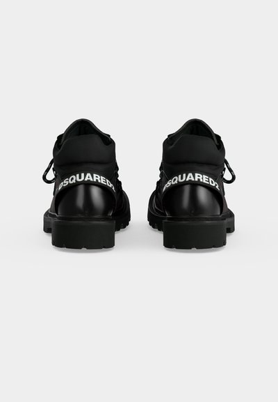 Paire de chaussures noires robustes avec semelles épaisses vues de dos, avec le logo "DSQUARED2" en blanc sur les brides de talon.